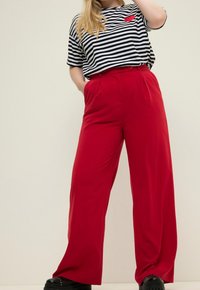 Czerwone spodnie z szerokimi nogawkami, gładka tkanina, z wysokim stanem i zakładkami, w zestawie z czarno-białym paskowanym krótkim rękawem z czerwonym sercem.