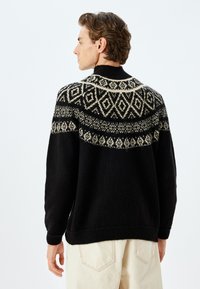 Zwarte gebreide trui met een hoge hals, met een crèmekleurig geometrisch patroon op de bovenrug en schouders.