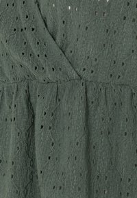 Dunkelgrünes Kleid aus strukturiertem Stoff mit kleinen Ausschnittmustern, weicher Oberfläche und gerafftem Taillenbereich für eine lockere Passform.