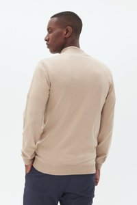 Bēškrāsas adīta džemperis ar garām piedurknēm, ar ribotu apkakli un apakšmalu. Mīksta tekstūra, pieguļošs dizains. Skats rāda aizmuguri ar minimālu detalizāciju.