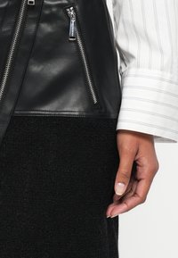 Μαύρο δερμάτινο μπουφάν με ασημένιες φερμουάρ, συνδυασμένο με ριγωτό άσπρο πουκάμισο και υφασμάτινη μαύρη φούστα, αναδεικνύοντας κομψά υλικά και αντίθετα χρώματα.