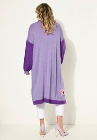 Lång cardigan i ljuslila med mörklila ärmar, med blommönster broderi och ribbad fåll. Slät textur.