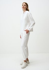 Witte hoodie met trekkoord, ontspannen pasvorm en lange mouwen, gecombineerd met aansluitende witte joggerbroeken. Zachte textuur, elastische manchetten en zakken.