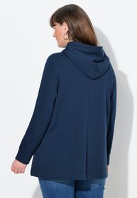 Sudadera con capucha en color azul marino, fabricada en un tejido suave. Presenta un corte relajado, mangas largas y un dobladillo cosido. Capucha visible con pliegues en la parte posterior.