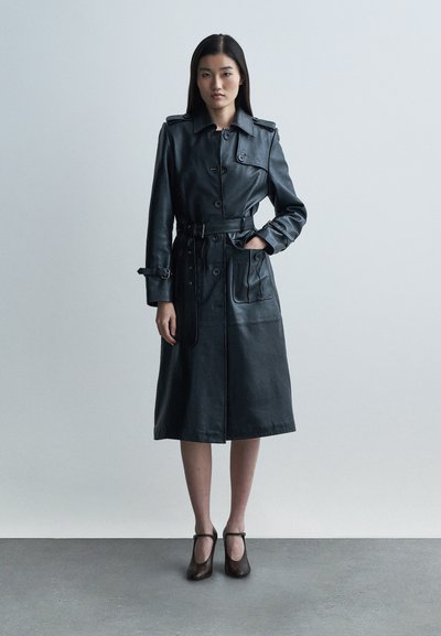 Crni kožni baloner s remenom u struku, velikim džepovima i kopčanjem na gumbe. Ima klasični ovratnik i dužinu do sredine lista.