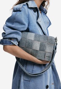 Dżinsowa torba na ramię o wzorze patchworkowym w odcieniach niebieskiego, z odpinanym paskiem i subtelnymi stębnowaniami. Gładka tekstura.