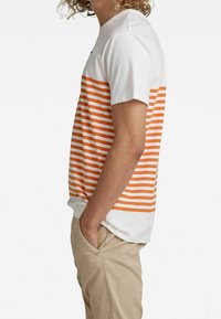 Kortærmet T-shirt i hvid med orange vandrette striber, med rund halsudskæring og afslappet pasform. Fremstillet af blødt bomuldsstof.