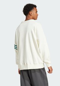 Vit sweatshirt med ribbade muddar och nederkant, som har gröna ränder på ena ärmen. Mjukt material, avslappnad passform och sänkt axelsöm.