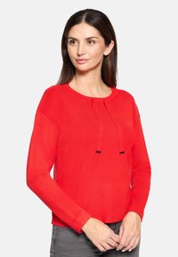 Czerwony sweter dzianinowy z długimi rękawami, okrągłym dekoltem i związaniami z przodu. Gładka tekstura i dopasowany krój. Udekorowany cienkimi czarnymi akcentami.