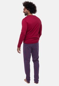 Röd långärmad skjorta gjord av mjukt tyg, kombinerad med byxor i blå och rosa ränder. Skjortan har en rund halsringning och åtsittande ärmar.