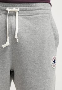 Pantalones de chándal grises confeccionados en una mezcla de algodón, con un cordón blanco, bolsillos laterales y una etiqueta de logotipo redonda con una estrella en el muslo izquierdo.
