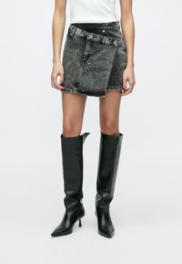 Fekete farmer miniszoknya magas derékkal, elöl zsebbel, övbújtatókkal és rojtos szegéllyel. Térdig érő, fényes fekete csizmával párosítva.