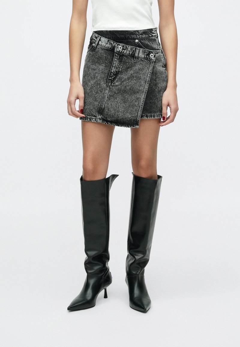 Fekete farmer miniszoknya magas derékkal, elöl zsebbel, övbújtatókkal és rojtos szegéllyel. Térdig érő, fényes fekete csizmával párosítva.