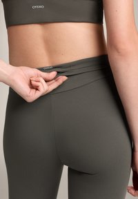 Oliwkowy zestaw odzieży sportowej składający się z krótkiego topu oraz legginsów z wysokim stanem, o gładkiej fakturze i detalem logo na pasie.