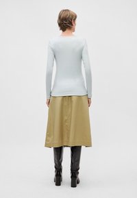 Camisa de manga longa azul-claro combinada com uma saia midi de cetim bege e botas altas até ao joelho pretas, vista por trás.