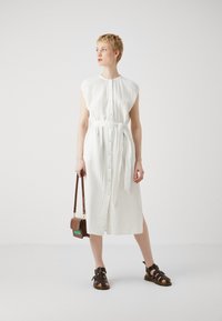 Rochie albă, până la genunchi, cu nasturi și curea de legat. Material texturat, mâneci scurte, asortată cu o geantă maro tip crossbody și sandale maro.