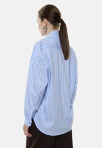 Camicia a righe azzurra chiaro con maniche lunghe, vestibilità comoda e orlo arrotondato. Caratterizzata da un colletto classico e polsini con bottone.