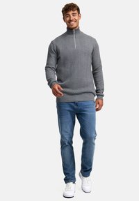 Grå zip-hals genser i et teksturert fiskebensmønster, kombinert med lyseblå jeans og hvite sneakers. Fittet silhuett med ribbede mansjetter.
