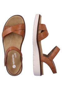 Sandales en cuir marron avec un design de bride entrecroisée, semelle intérieure douce et semelle extérieure blanche rembourrée avec un motif de semelle.