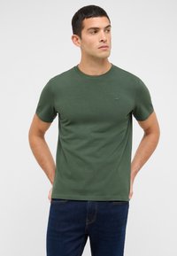 Zielona bawełniana koszulka z krótkim rękawem i okrągłym dekoltem, z subtelnym logo na piersi. W zestawie z ciemnoniebieskimi jeansami.