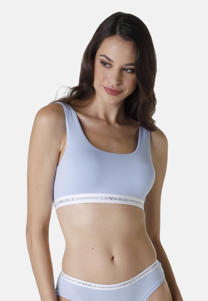 Bralette azzurro chiaro realizzato in tessuto morbido, con una ampia fascia elastica bianca con il logo "LOVABLE". Design semplice, senza maniche.