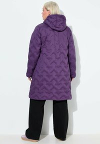 Abrigo acolchado morado con capucha, que presenta un patrón acolchado y mangas largas. Combinado con pantalones negros y calzado de un morado claro.