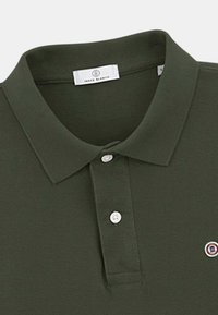 Polo vert foncé avec un col, trois boutons et un petit patch logo sur la poitrine. Fabriqué en tissu texturé.