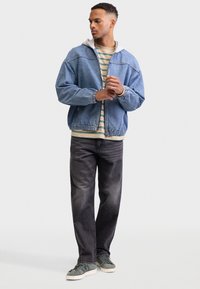 Τζιν μπουφάν με γκρι κουκούλα, ριγέ πουκάμισο από κάτω, μαύρο τζιν και πράσινα αθλητικά παπούτσια. Καθημερινή ένδυση με αντιθετικές υφές και χρώματα.