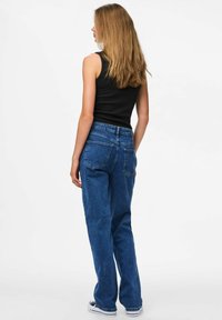 Fitted black tank top and high-waisted blue denim jeans, medium wash, relaxed fit, visible back pockets, paired with black and white sneakers.