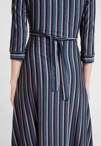 Robe rayée avec des rayures verticales bleu marine, crème et bleues, dotée d'une taille à nouer, de manches trois-quarts et d'une silhouette fluide.
