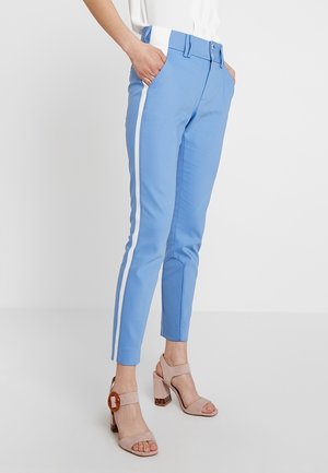 Pantaloni azzurri chiari con strisce laterali bianche, vestibilità su misura, passanti per cintura e tasche frontali. Abbinati a sandali beige con tacco a blocco.