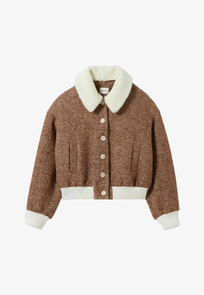 Giacca marrone a spina di pesce tagliata con colletto in pelle ecologica bianca, orlo e polsini a coste, e chiusura a cinque bottoni. Presenta due tasche laterali.