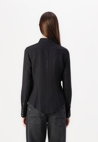 Black button-up shirt with textured pattern, featuring a pointed collar and long sleeves, paired with dark gray baggy jeans.