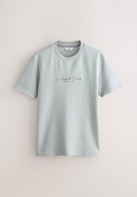 Világoszöld rövid ujjú póló, sima anyagból készült, kerek nyakkal és díszes betűtípussal hímzett felirattal az elején.