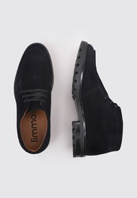 Zapatos de ante negro con un acabado suave, presentan punteras redondeadas, cordones y una suela de goma negra texturada con ranuras.