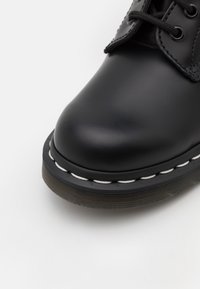 Stivale in pelle nera con punta rotonda, suola spessa, dettagli di cucitura bianca e design con lacci in corda scuri.