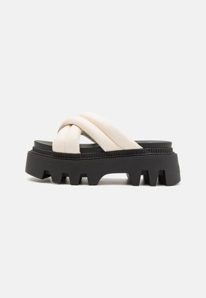 Sandali platform con suola in gomma nera e fascetta incrociata color crema, dotati di battistrada spesso e dettagli testurizzati sulla suola.