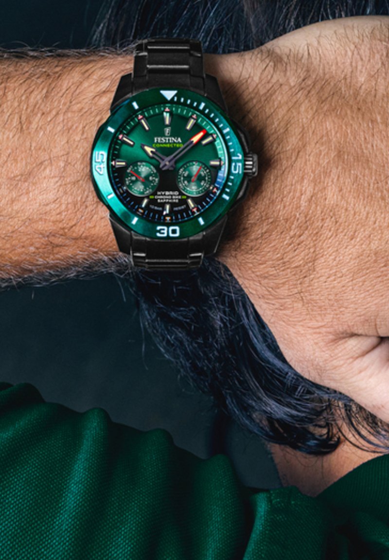 Montre en métal noir avec un cadran et une lunette verte. Elle présente de grands index, des sous-cadrans et des aiguilles luminescentes. Les bracelets sont en maillons métalliques.