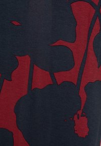 Grafické tričko s tmavě námořnickým základem a výrazným červeným abstraktním vzorem, vyrobené z měkké bavlny a s krátkými rukávy.