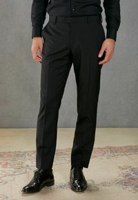 Schwarze Hose mit einem maßgeschneiderten, geraden Schnitt, die ein dezentes Nadelstreifenmuster und einen eng anliegenden Bund aufweist, kombiniert mit schwarzen Sch dressschuhen.