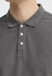 Gray polo shirt with a textured fabric, featuring a collar, three white buttons, and a subtle embroidered logo on the left side.