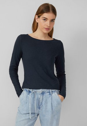 Langarmige marineblauwe top met een bootnek, gemaakt van gestructureerde stof, gecombineerd met lichtblauwe high-waisted jeans met een trekkoord.