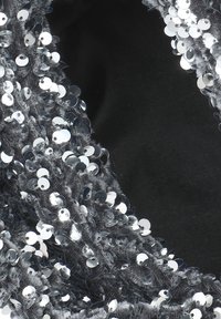 Silverpaljettyg med en texturerad svart baksida, som har rundade, reflekterande paljetter tätt placerade längs en mjuk, plyschyta.