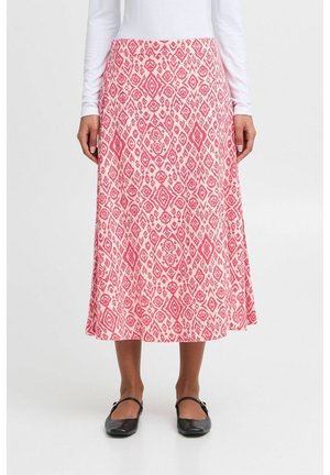Kobieta nosząca różowo-białą spódnicę midi w wzory, do której dobrano czarne buty typu Mary Jane oraz biały top z długim rękawem.