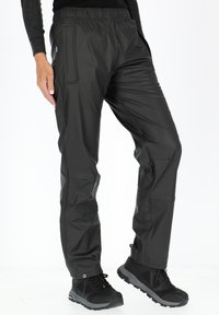 Zwarte, waterdichte broek met een elastische tailleband, zijrits- sluitzakken en een tapered fit. De stof lijkt glad met een matte afwerking.