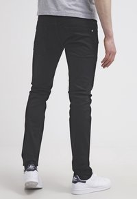 Černé džíny slim fit, s pěti kapsami a jemnou texturou. Kombinované s bílými teniskami Adidas s modrými detaily.