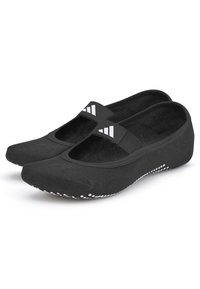 Zapatos negros sin cordones con un diseño texturizado, parte superior de tela y una suela de goma con acentos blancos en forma de puntos. Incluye una banda elástica ancha a lo largo del empeine.