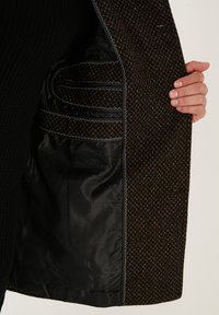 Wollmantel mit einem strukturierten braunen Außenstoff und einem glatten schwarzen Futter, ausgestattet mit Innentaschen und kontrastierenden Nähten.