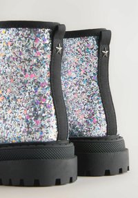Bottines à paillettes avec une tige en tissu noir, ornées de paillettes argentées et multicolores. Semelle épaisse en caoutchouc noir avec un motif texturé.