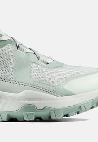 Lys grøn atletik sko med en mesh-overdel, tekstureret gummisål og lagdelt design med en blanding af glatte og mønstrede materialer.